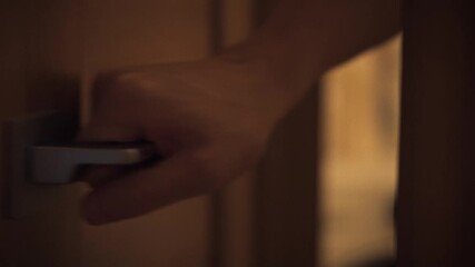 A close-up of a man grabbing the handle of an interior door. He slowly opens it, moving into another part of the house. The cozy lighting creates an atmosphere of warmth and calm