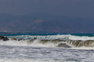 Mediterranean Sea waves rolling on the sandy beach of Cyprus with mountains in the background.