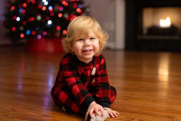 Smiling child in plaid pajamas by Christmas tree and fireplace