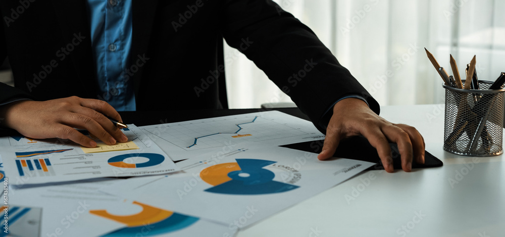 Poster a focused business professional reviews various charts and graphs on a desk, utilizing a digital tab