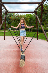 Young girl balancing on rope bridge in park. A young girl carefully walks across a suspended rope...