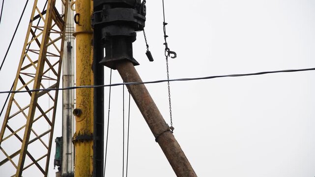 Close-up view of pile driver picking up concrete pile at a construction site before hammering. Overcast sky. Real time video. Deep foundation theme.
