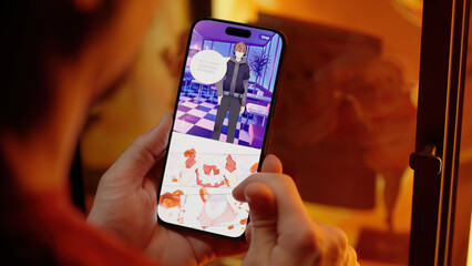Reading colored maid girls digital manhwa comic webtoon on smartphone beside merchandise with figurines, over shoulder view