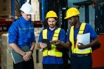 Warehouse workers from different ethnic backgrounds standing together inside storage area checking...