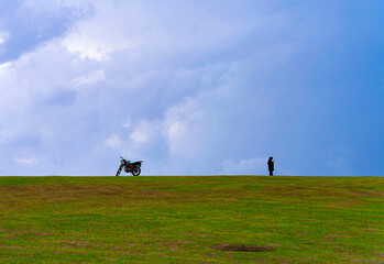 Silhouette of man and motorcycle on grassy hill under dramatic cloudy sky