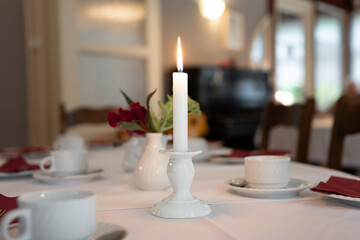 Shining candle on a dinner table. Elegant light at an event location. Celebrating a birthday, wedding or anniversary with the family. Cozy decorated place to feel comfortable.