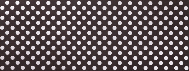 Black background from wrapping paper with white polka dot pattern. Texture of dark brown dotted paper backdrop