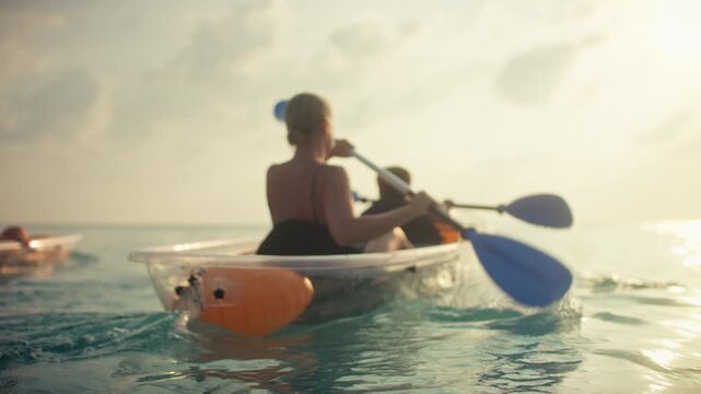 Enjoying a serene kayaking experience in transparent boats on the clear ocean, a family paddles together during golden hour. Perfect for tropical vacations, peaceful moments, and aquatic adventures.