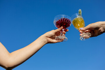 Friends celebrating a joyful moment together while toasting with colorful drinks against a clear blue sky