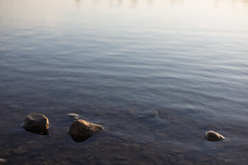 Serene water surface with smooth stones partially submerged during early morning light near a tranquil lake