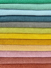 A vibrant display of colourful fabric pieces like towels stacked neatly on top of each other. Represents textile variety, fashion materials, and creative design resources.