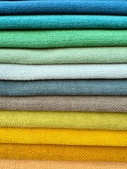 A vibrant display of colourful fabric pieces like towels stacked neatly on top of each other. Represents textile variety, fashion materials, and creative design resources.