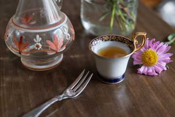 Elegant tea setup with floral accents on wooden table featuring a delicate cup of tea and a fork beside a glass vase