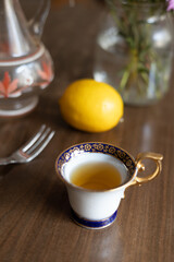 Delicate porcelain cup filled with herbal tea beside a fresh lemon and elegant glass vase on a wooden table