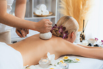 Hot herbal ball spa massage body treatment, masseur gently compresses herb bag on woman body....