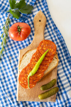 Slices of spicy chorizo laid on a slice of bread with fresh vegetables on a blue checkered cloth background