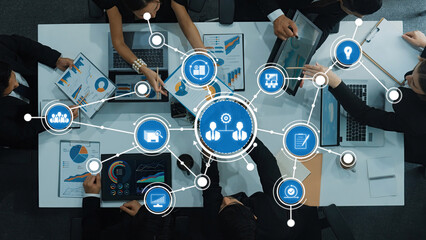 A top-down view of a business team collaborating over data analytics, with charts and graphs displayed on screens, emphasizing teamwork and strategic planning in a modern workspace. Amity