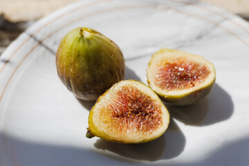Fresh figs on a white plate with one whole and one sliced depicting their juicy interior in warm sunlight