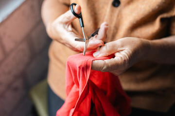 Hands skillfully cutting red fabric in a bright indoor space during afternoon sunlight, showcasing...