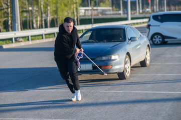 Caucasian man pulling a car with a rope. 