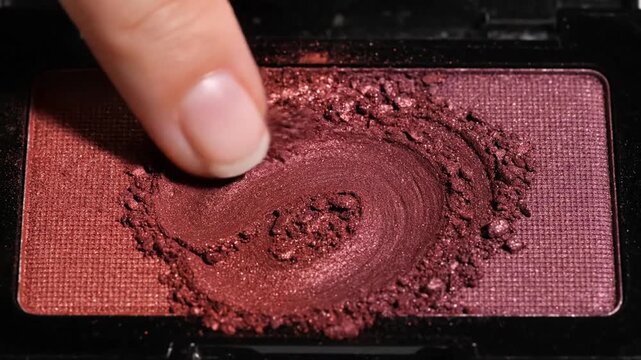 Close-up of a finger swirling vibrant reddish-brown eyeshadow, showcasing its texture and color in a rectangular compact