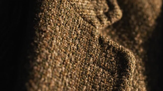 Close-up texture of brown tweed fabric with dramatic lighting creating shadows and highlighting the weave pattern