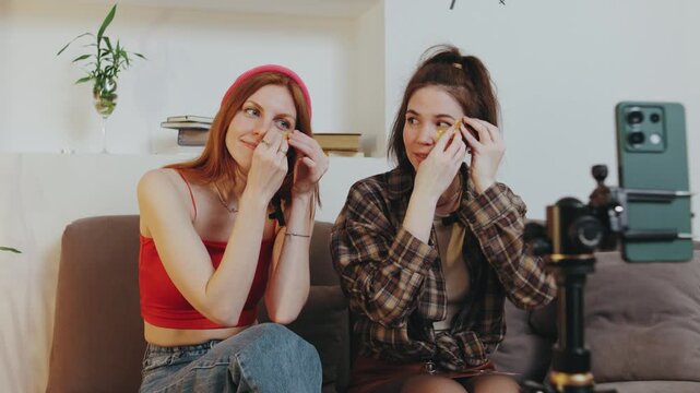 Friends sharing beauty tips and makeup techniques while recording a tutorial in a cozy living room setting