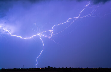 A powerful lightning bolt vividly lights up the evening sky over a plain landscape. The striking...