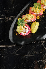 Close-up of sushi rolls combining salmon, mango, cucumber, and cream cheese inside rice and nori. Topped with thin salmon slices