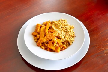 A classic Brazilian dish known as dobradinha, prepared with beef tripe, white beans, and tropical spices, served with traditional farofa made from toasted cassava flour.
