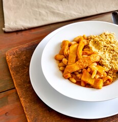 A classic Brazilian dish known as dobradinha, prepared with beef tripe, white beans, and tropical spices, served with traditional farofa made from toasted cassava flour.