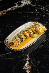 Close-up of sushi rolls combining salmon, mango, cucumber, and cream cheese inside rice and nori. Topped with thin salmon slices 