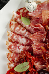 Assorted charcuterie board with a variety of cured meats, cheeses, and vegetables. Slices of salami, prosciutto, and chorizo served with blue cheese, brie, hard cheese cubes, olives, sun-dried tomatoe