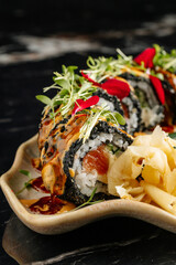 Close-up of sushi rolls combining salmon, mango, cucumber, and cream cheese inside rice and nori. Topped with thin salmon slices and a drizzle of spicy mayo