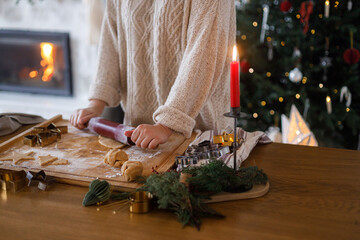 Woman making gingerbread christmas cookies. Hands holding gingerbread dough, rolling pin and metal cutters on rustic table on background of christmas tree. Winter holiday preparation
