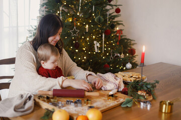 Happy mother with cute baby son making gingerbread christmas cookies together on background of...