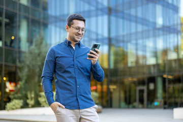 Professional man using smartphone outside a modern glass office building