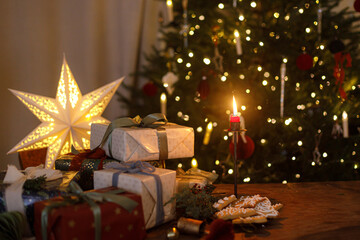 Stylish christmas presents, ornaments, gingerbread cookies and candle on table on background of...
