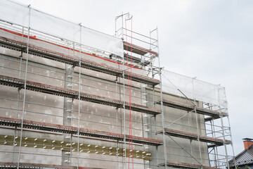 Large building under construction covered with scaffolding and safety net, showing urban development, construction process, renovation, industrial structure, and modern growth