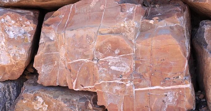 Closeup squarish pink smooth surface rock with white mineral veins near black rocks 4k