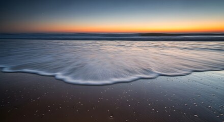 Serene ocean waves gently kiss sandy beach at twilight, creating a tranquil coastal escape.