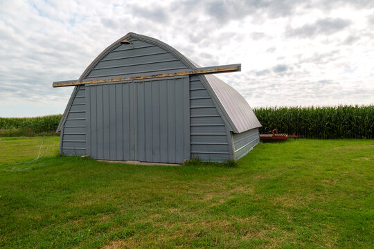 Metal Quonset Hut on Rural Farmyard with Cornfield Background &ndash; Agricultural Storage Building
