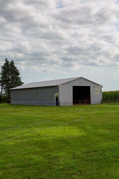 Gray Metal Pole Barn Farm Shed With Sliding Door Open Surrounded by Green Mowed Grass and a Tasseled Cornfield