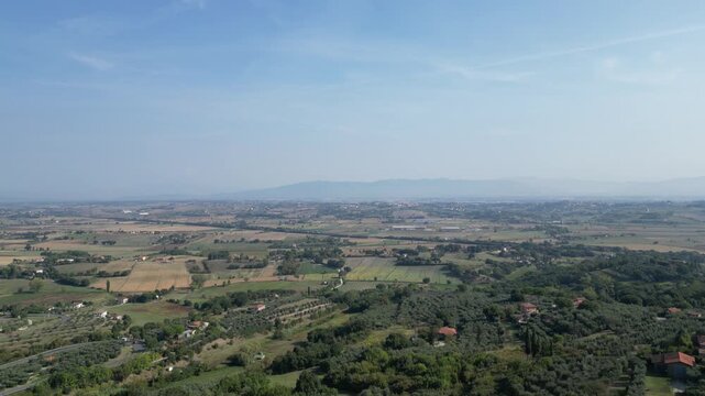 Drone flying over the Valdichiana valley starting from the hilltop town of Lucignano, Tuscany, Italy. Sunny summer landscape with fields, hills and countryside.