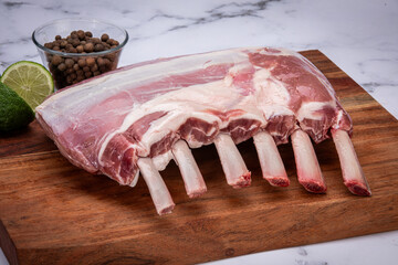 Close-up of raw lamb chops on a wooden cutting board with pepper and lime in background