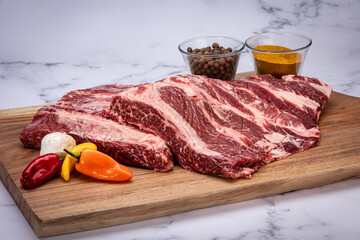 raw beef steak on wood cutting table with spices on a white marble background