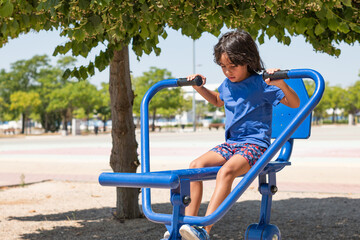 Young boy exercising on blue equipment in a park