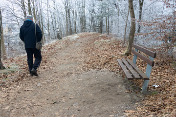 A man walks along a frosty path past a wooden bench in a winter park