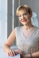 Portrait of smiling woman in festive clothes against a gray wall in a bright sunny room. Vertical photo