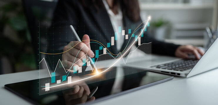 A business professional closely examines stock market trends using a digital graph on a tablet, alongside a laptop in a modern office setting. Impute - Powered by Adobe